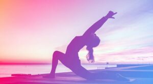 A person is doing a yoga pose in which they bend backwards and stretch their arms in the air. The background shows a sunset by the sea, with a purple-pink color gradient.