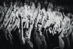 Crowd of people with raised arms, some with closed eyes, expressing enthusiasm and participation. The scene is in black and white, which lends the picture a solemn atmosphere.