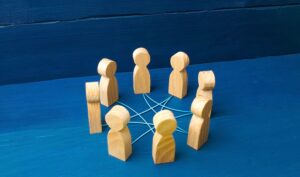 Wooden figures stand in a circle on a blue surface, connected by blue threads. Each figure stands for a network or community in a separate, quiet environment.
