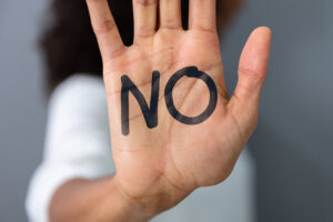 One hand is facing forward with the palm of the hand on which the word NO is written. The background is neutral, putting the focus on the clear message.