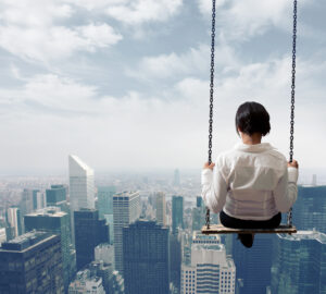A person in a white shirt sways high above a skyline of skyscrapers. The sky is slightly cloudy and the city stretches out in the background.