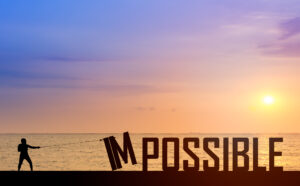 A silhouette pulls on a rope to knock over the letter I of IMPOSSIBLE while the sun rises or sets over the sea. The sky is pastel-colored.
