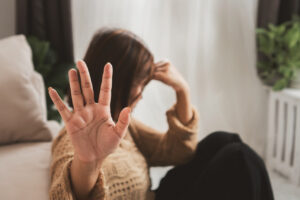 Eine Frau hat sich vor ihre Couch gekniet und scheint ersch&ouml;pft. M&ouml;glicherweise machen sich bei ihr Symptome von Burnout oder Depression bemerkbar.